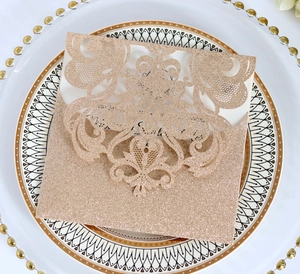 Champagne gold glitter invitation card with laser cut lace patterns on a white plate