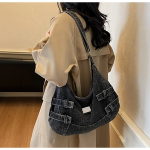 Detail of dark washed denim messenger bag with metallic buckles and adjustable strap