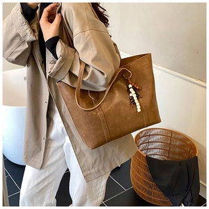 Detail of a brown retro tote bag with wooden bead charm on a beige trench coat