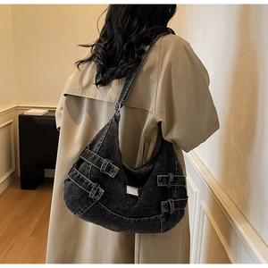 Detail of black denim hobo bag featuring silver buckles and metallic brand plate