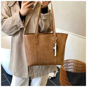 Detailed view of a vintage brown tote bag with beaded charm and embossed lettering