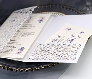 Macro shot of laser-cut white wedding invitation with elegant purple floral inner card