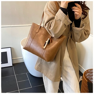 Brown vintage tote bag with contrast beaded charm shown in a minimalist interior setting