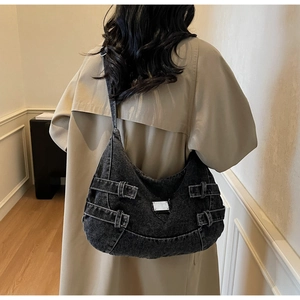 Model wearing large black denim hobo crossbody bag with silver buckles and a long beige coat
