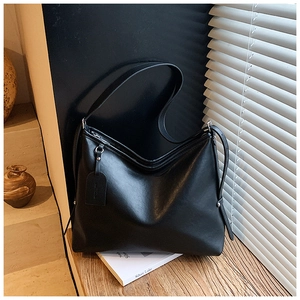 Detail of minimalist black leather crossbody bag on a textured wooden surface with soft light