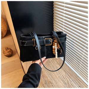 Détail du sac à bandoulière noir mat avec boucle dorée et pendentif en perles