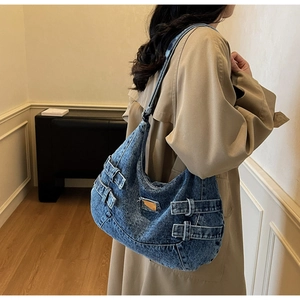 Detail view of large blue washed denim messenger bag featuring metal buckle and retro style