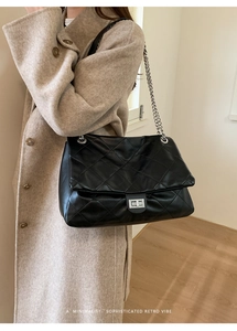 Close-up of black quilted leather tote with silver metal twist lock and chain strap