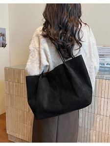 Grand sac cabas noir en daim avec fines lanières porté comme un sac à bandoulière sous le bras