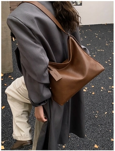 Detail view of brown leather tote bag with wide strap and side brand tag on a hobo design