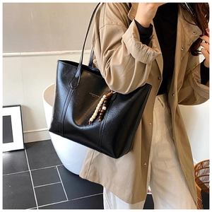 Detail of black wax leather tote bag with gold logo and beaded tassel charm on a beige coat