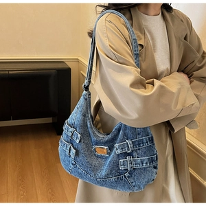 Detail of blue washed denim shoulder bag with metal logo and vintage buckle straps