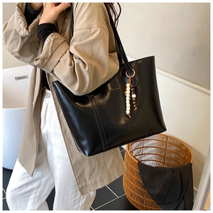 Detail of black wax leather tote bag featuring a decorative beaded tassel charm