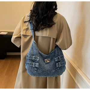 Détail d'un grand sac bandoulière en denim bleu avec sangle latérale et plaque en métal