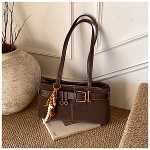 Gros plan du sac marron vintage avec boucle dorée et détail de pompon en perles de bois