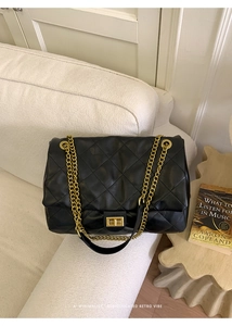 Macro detail of quilted black leather texture and gold chain strap on a tote bag