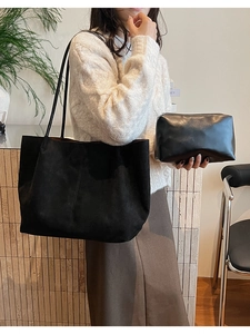 Détail d'un sac cabas en daim noir et pochette en cuir dans une scène intérieure chaleureuse