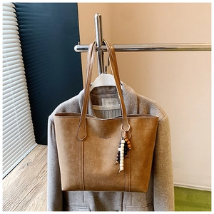 Close-up of brown faux leather tote bag with vintage texture and wooden bead pendant detail