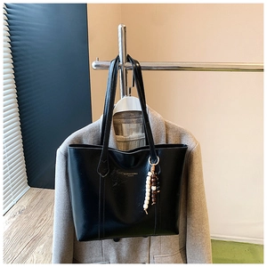 Detailed view of black faux leather tote bag with beaded tassel and shoulder strap