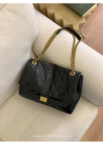 Close-up of black quilted tote bag with gold chain strap on an elegant sofa