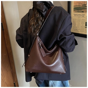 Detail view of large dark brown leather tote bag with side drawstrings and metal rivets