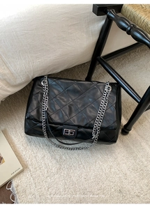 Detail of black quilted leather tote with silver chain strap on a textured rug