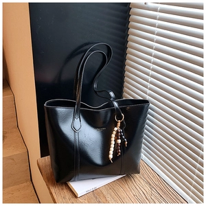 Detail of black faux leather tote bag with gold lettering and colorful beaded tassel