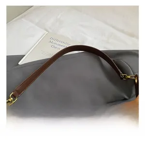 Détail du sac sous le bras en tissu gris avec bandoulière en cuir marron et crochet doré