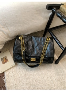 Macro shot of black quilted leather texture and gold metal chain strap on a tote bag