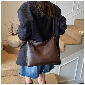 Detail view of a large brown leather hobo bag worn by a model in a minimalist setting