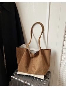 Détail d'un grand cabas en daim caramel posé sur une valise argentée pour le voyage