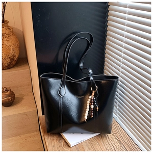 Detail of black faux leather tote bag with wooden bead charm and brand lettering