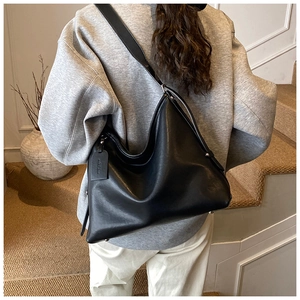 Detail of minimalist black leather hobo bag featuring silver rivets and wide strap