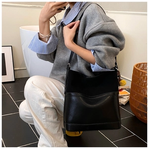 Detail of a large black matte leather bucket bag with a yellow pompom charm on a model