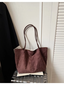 Détail du grand sac cabas en daim bordeaux avec grande capacité sur une valise argentée