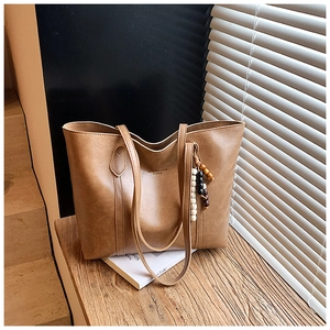 Detail of a brown vintage leather tote bag featuring a colorful wooden bead pendant