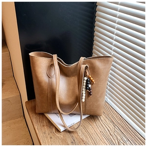 Detail of vintage brown leather tote bag with wooden bead charm in natural sunlight