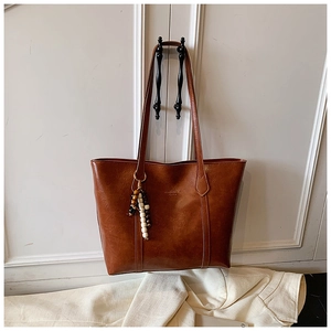 Detail of vintage brown tote bag with beaded tassel hanging on a white classic door