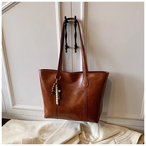 Detail of brown faux leather tote bag with unique beaded tassel and brand embossing