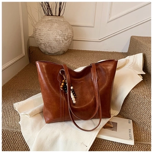 Brown leather tote bag with a beaded tassel and brand logo on white stairs