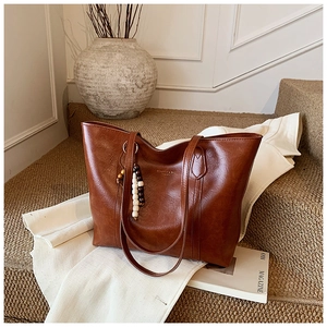 Detailed close-up of brown vintage leather tote bag with elegant beaded pendant and gold logo
