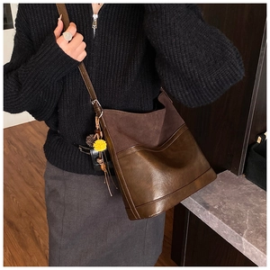 Detailed view of dark brown bucket bag with contrasting textures and yellow pom pom