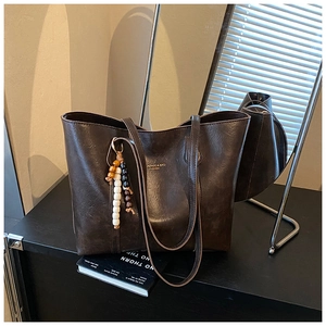 Detail of vintage brown tote bag with beaded charm and polished faux leather texture
