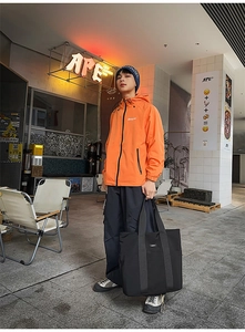 Close-up of a large black nylon tote bag styled with an orange hooded windbreaker jacket