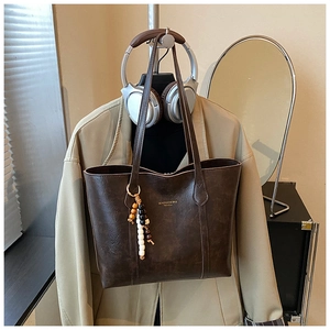 Macro view of dark brown faux leather tote bag with SOAZHUO text and beaded charm