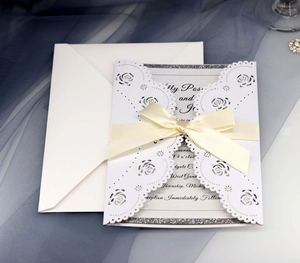 Detail of laser-cut rose hollow wedding invitation with cream ribbon and envelope