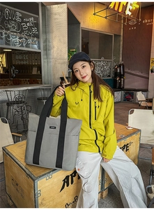 Detail of a large grey commuter tote bag with black straps in a street fashion setting