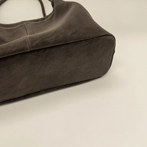 Macro view of dark brown leather shoulder bag featuring detailed white contrast stitching