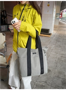 Outdoor street shot of a large gray tote bag with black straps and side pockets