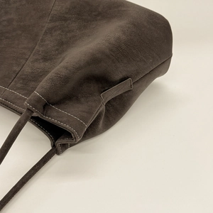 Detail of dark brown suede tote bag showing precision stitching and reinforced handle joints